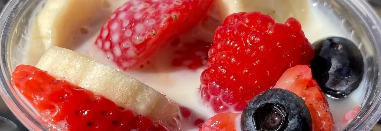 A cup of sliced strawberries, banana, raspberries, and blueberries in cream.