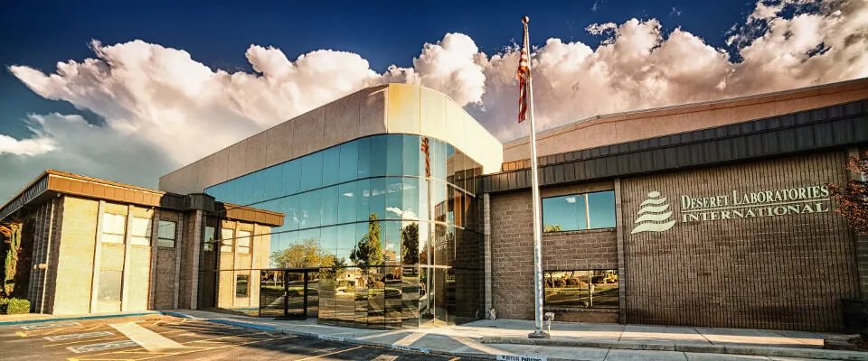The Deseret Laboratories International building, a brick and glass office under a bright sky with the U.S. flag out front.