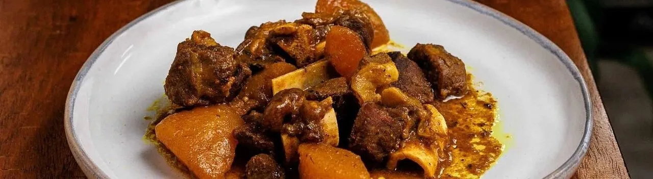 A white plate of Jamaican curry with braised meat and chunks of squash in a rich sauce.