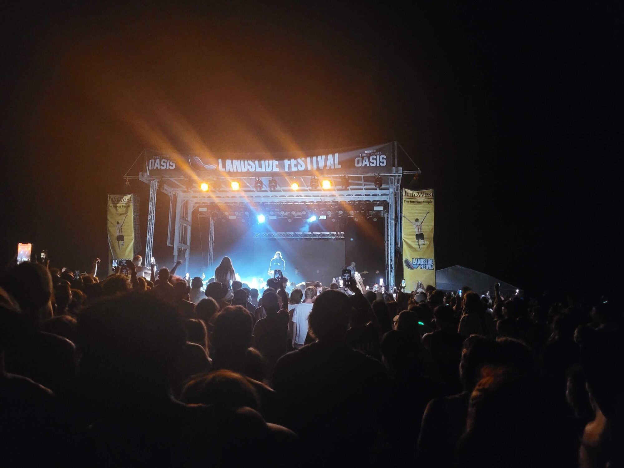 A nighttime crowd at Landslide Festival facing a lit stage flanked by InfoWest banners