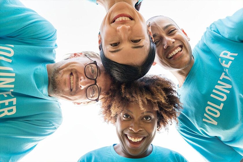 Four volunteers in blue shirts smiling in a huddle seen from below
