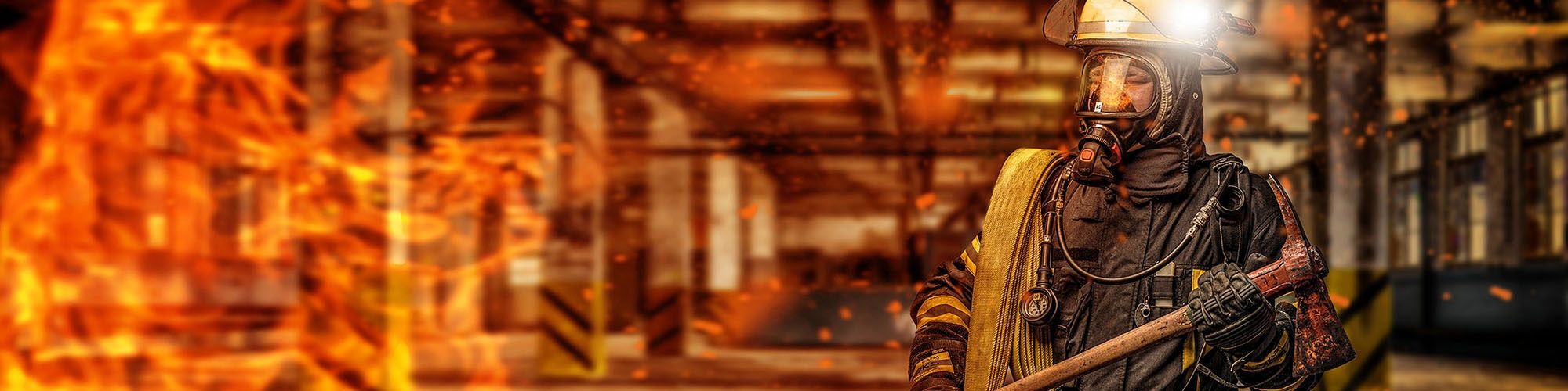 A firefighter in full turnout gear carrying an axe through a smoke-filled structure