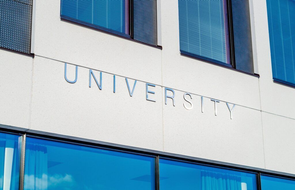 Sunlit university building with metal UNIVERSITY lettering above ground-floor windows