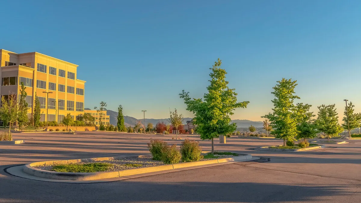 A modern office building beside a landscaped parking lot at golden hour, with Utah mountains behind.