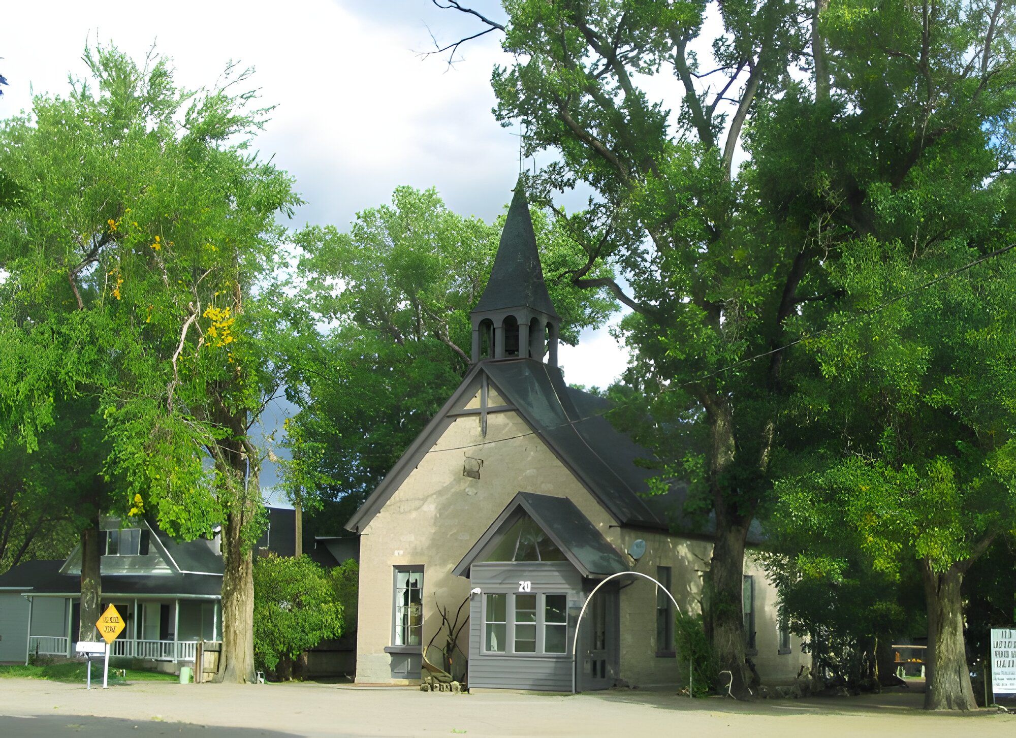 A historic stone church with a wooden bell tower under tall trees in Monroe.