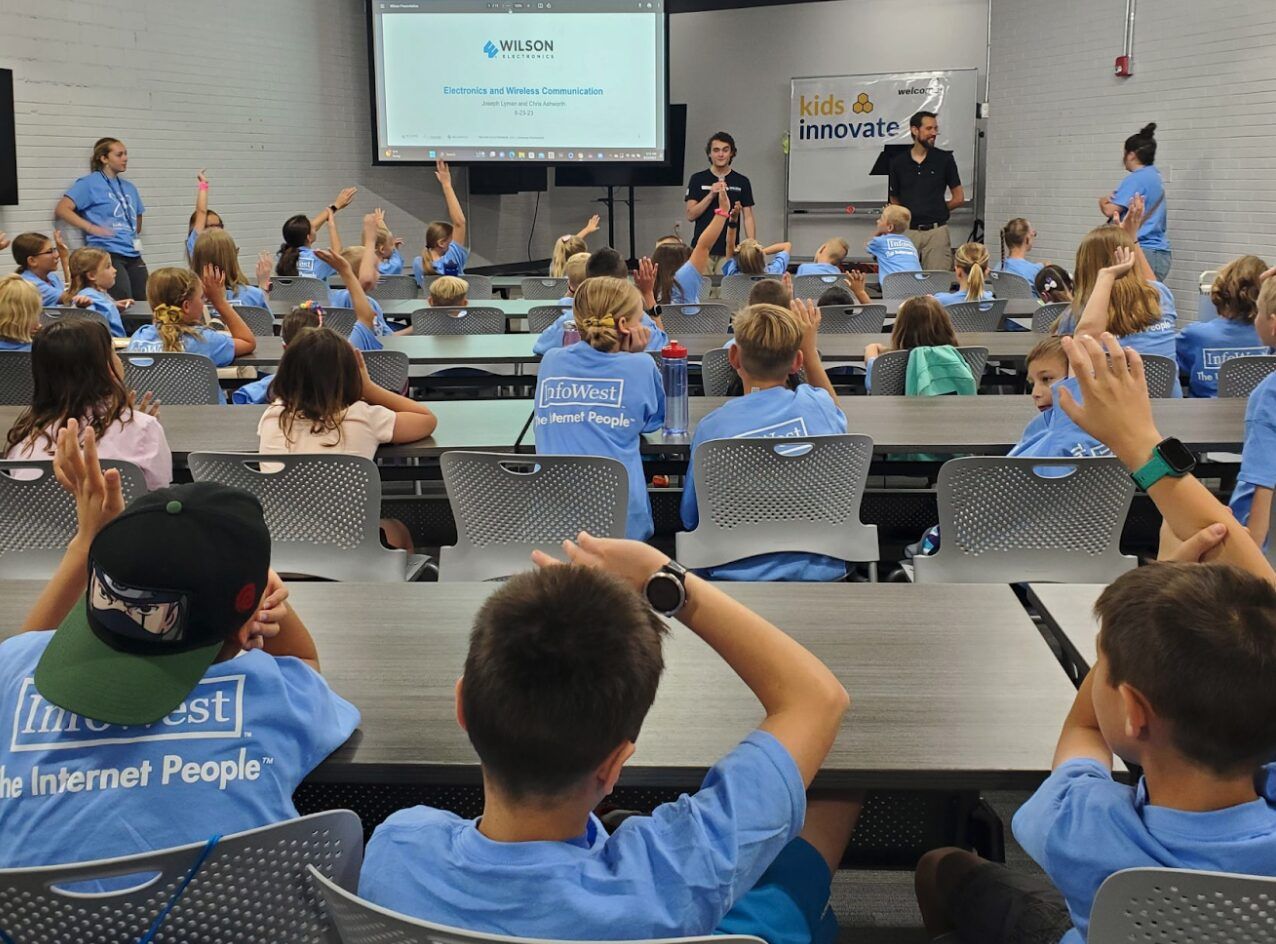 A room of kids in InfoWest shirts raising their hands during a Kids Innovate session