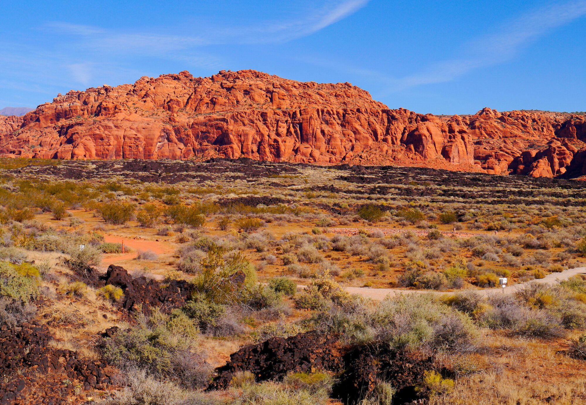 Red cliffs above black lava rock and desert brush in Washington County, Utah.