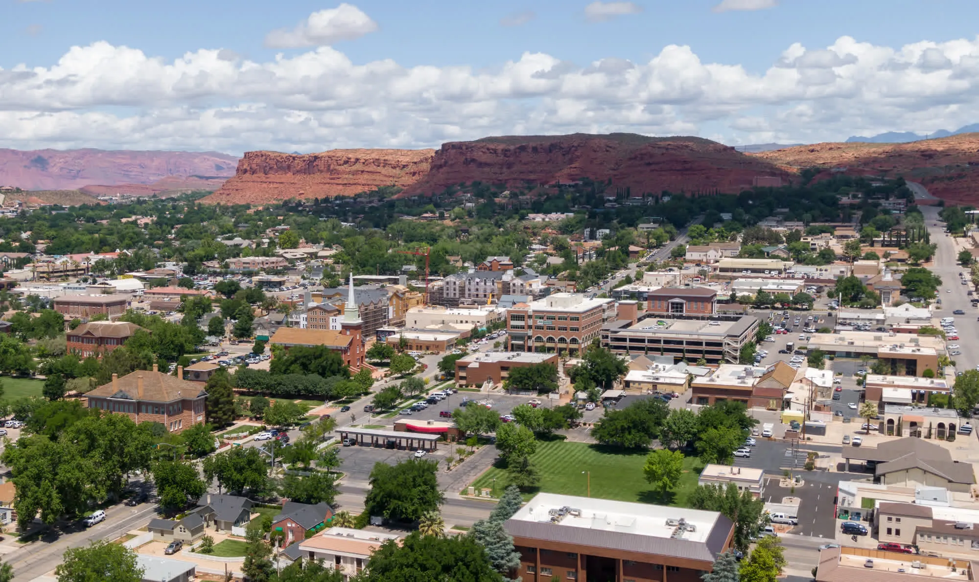 Aerial view of downtown St. George with red sandstone cliffs rising behind the rooftops.