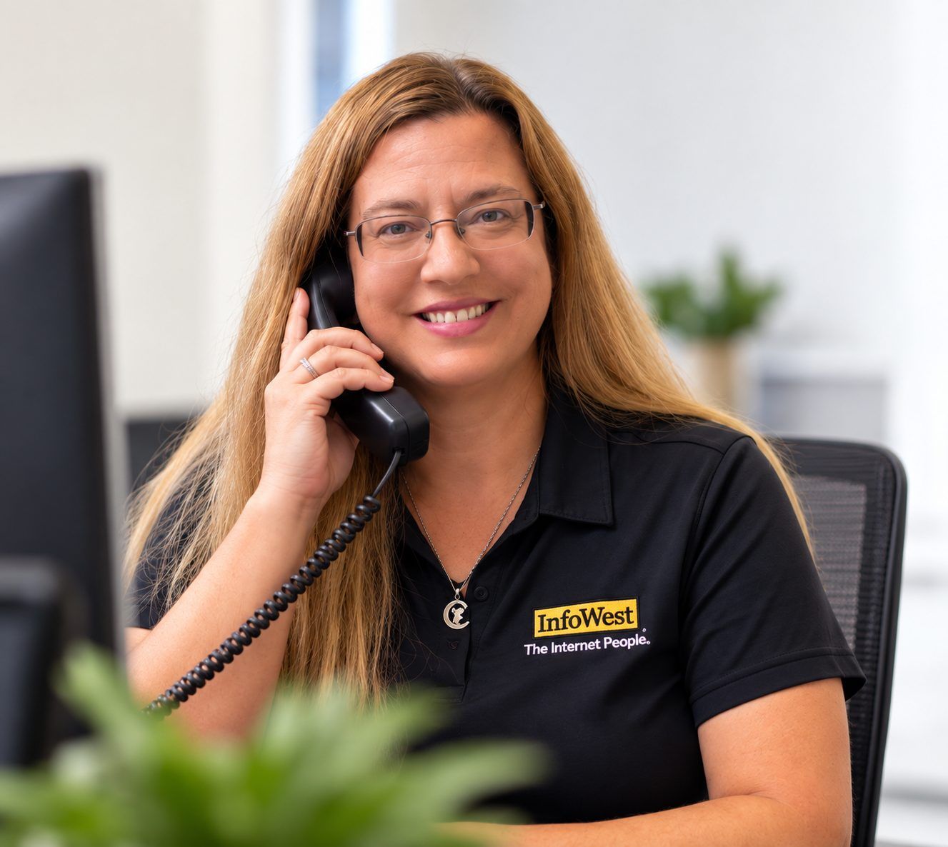 An InfoWest team member smiling on a desk phone at the office
